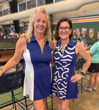 Two women in moorlow blue and white athletic pickleball dresses standing together in an indoor setting.
