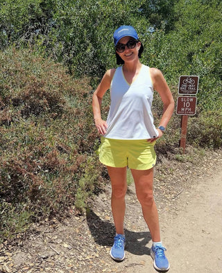 Woman in moorlow athletic wear standing on a trail with a sign in the background